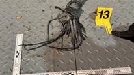 A broken, frayed cable on a metal floor with a ruler and a yellow plastic sign with the number 13.