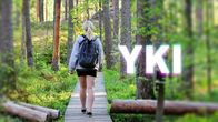 Nainen kävelee metsässä pitkospuilla, kuvan päällä on YKI-teksti.