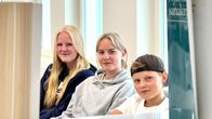 Kolme koululaista istuu, kuvan reunoilla näkyy kirjoja.