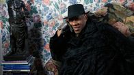 Muotitoimittaja André Leon Talley istuu mustassa viitassa kukikkaan tapetin peittämän seinän edessä. Kuva dokumenttielokuvasta.