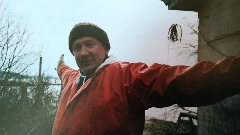Jari Dahlström i röd jacka och grön mössa står utomhus med armarna utsträckta.
