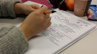 En student gör anteckningar i sitt häfte på två språk.
