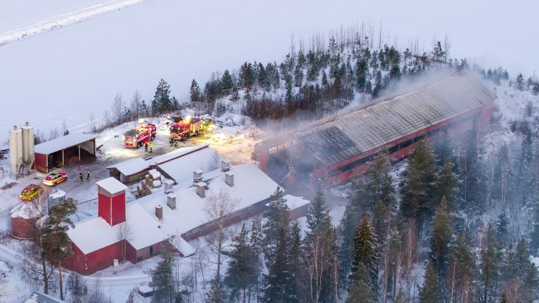 Navetta palaa Kouvolassa. Ilmakuvassa näkyy savuava raunio navetasta.