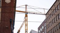 Tampereen keskustassa kerrostalojen yläpuolelle nouseva oranssi rakennusnosturi.