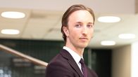 Ilmari Nurminen seisoo kaarevassa portaikossa tumma puku päällään kädet ristissä ja katsoo kameraan.