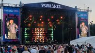 Esiintyjä laulaa lavalla värikkäiden valojen loisteessa suurelle yleisölle, taustalla lukee "PORI JAZZ 2026".