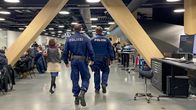 Harmaassa tilassa näkyy työskentelypöytiä kummallakin sivustalla ja näiden välissä kävelee kirjaston työntekijä kahden poliisin kanssa.