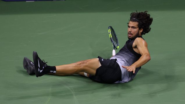 Tennispelaaja pyllähtäneenä maahan maila kädessään.