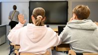 Photo shows two teenagers sitting in a school classroom.