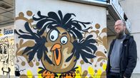 Savonlinnalainen graffitiharrastaja Toni Korhola hymyilee maalaamansa lintugraffitin luona Kauppalinnan edustalla.