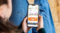 En person skrollar på en nätsida på sin mobiltelefon. Personen har brunt hår och blåa jeans på sig. 