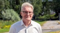 Mies jolla on vaalea paita , katsoo kameraan. Taustalla näkyy koivuja.