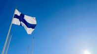 Photo shows the Finnish flag flying from a flagpole with a clear blue sky in the background.