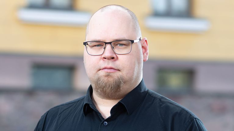 Mies seisoo ulkona pukeutuneena mustaan kauluspaitaan.