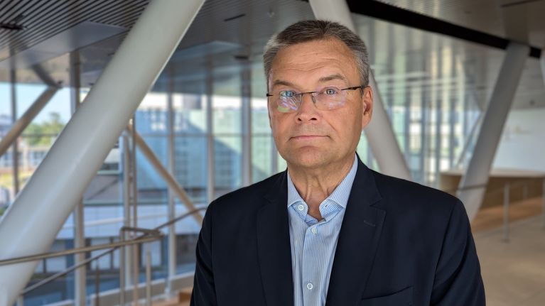 Vanhempi mieshenkilö seisoo sairaalarakennuksen käytävällä.