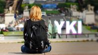 Nainen istuu portailla ja katsoo eiffel-tornille päin, kuvan päällä YKI-teksti.