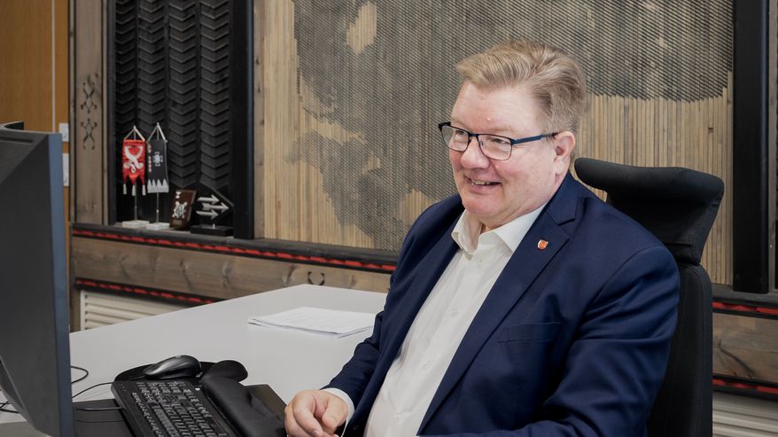 Konneveden kunnanjohtaja  Mika Pasanen istuu työpöytänsä ääressä. Hänen takanaan on suuri puurimoista valmistettu metson kuva.