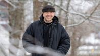  Henkilö, jolla on yllään tumma talvitakki ja pipo, seisoo lumisessa metsäisessä ympäristössä.