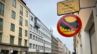 Ett trafikmärke fäst på en vägg längs en gata med bilar.