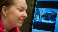 Matleena Haapakoski tietokoneella. Taustalla näkyy televisio johon on peilattu tietokoneen näyttö. Televisiossa näkyy kuinka tekoäly tutkii kasvoja.