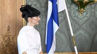 Suzanne Innes-Stubb  kuuntelee valkoisessa asussa päässään musta hattu.