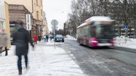 Buss kör längs gata med folk promenerande längs trottoar