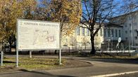Suuri opastaulu, jossa lukee "Kimpisen koulukeskus", seisoo koulurakennuksen ja lehtipuiden edessä.