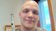 Henkilö pitää hopeista huilua sisätiloissa ikkunan vieressä, taustalla näkyy rakennuksia.