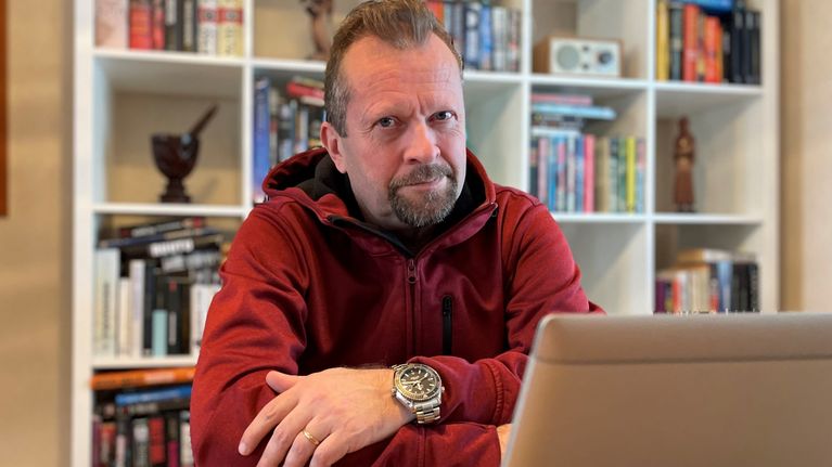Punaiseen huppariin pukeutunut mies istuu ja nojaa käsiään pöytään.