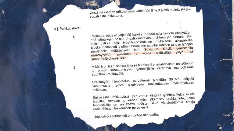 Revitty pala paperia tummansinisen kuluneen taustan päällä. Paperissa on tekstiä, josta on korostettu oranssilla tussilla teksti: ” Sovittuun, tietyllä perusteella määräytyvään palkkaan ei voida sisällyttää ylityö- tai sunnuntaikorvauksia.