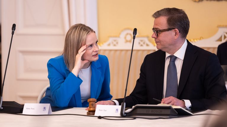Riikka Purra ja Petteri Orpo istuvat pöydän ääressä ja keskustelevat tiiviisti.