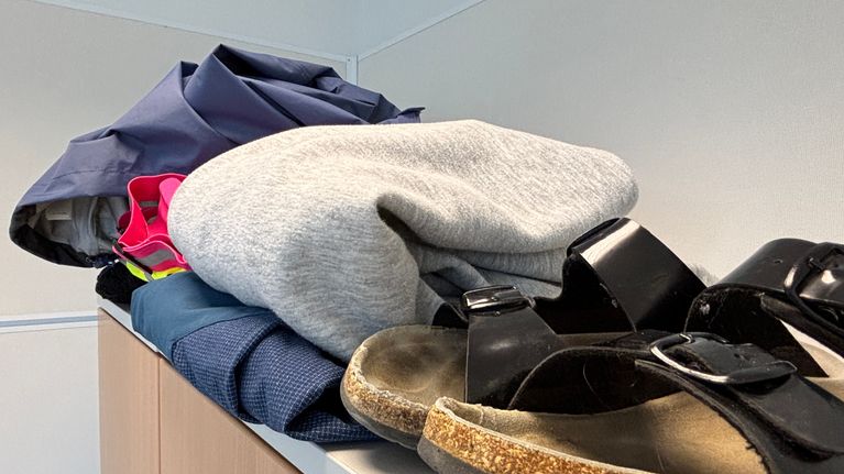 Ett par svarta sandaler och en hög kläder ligger ovanpå ett skåp.