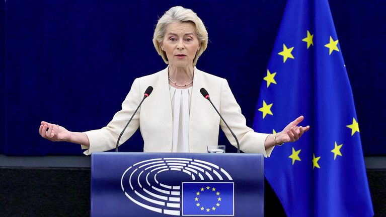 Nainen seisoo puhujakorokkeen takana mikrofonien edessä, taustalla EU:n lippuja ja Euroopan parlamentin logo.