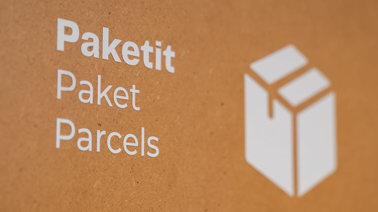 Brun väggyta med vit text: "Paketit Paket Parcels".