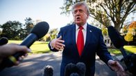 Donald Trump pukeutuneena tummansiniseen pukuun ja punaiseen kravattiin puhuu useiden mikrofonien edessä ulkona.