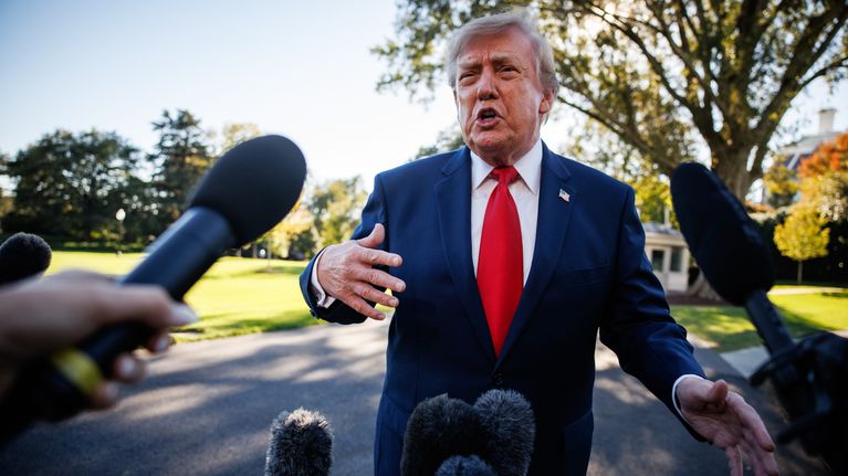 Donald Trump pukeutuneena tummansiniseen pukuun ja punaiseen kravattiin puhuu useiden mikrofonien edessä ulkona.