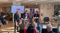 Tre personer står framför en folksamling; en av dem klipper ett rött band.