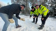 Tre män i vinterkläder står och visar upp snö i sina händer på ett skidspår.