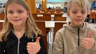Tyttö ja poika istuvat ruokapöydän ääressä ja näyttävät peukkua kouluruoalle.