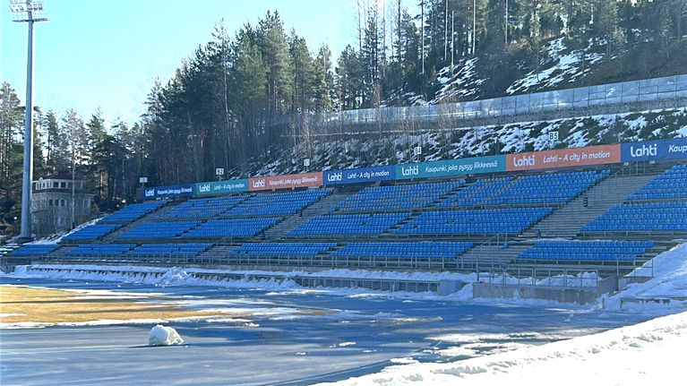 Kuvassa on urheilukentän katsomo, jossa on sinisiä muovipenkkejä vierekkäin. 