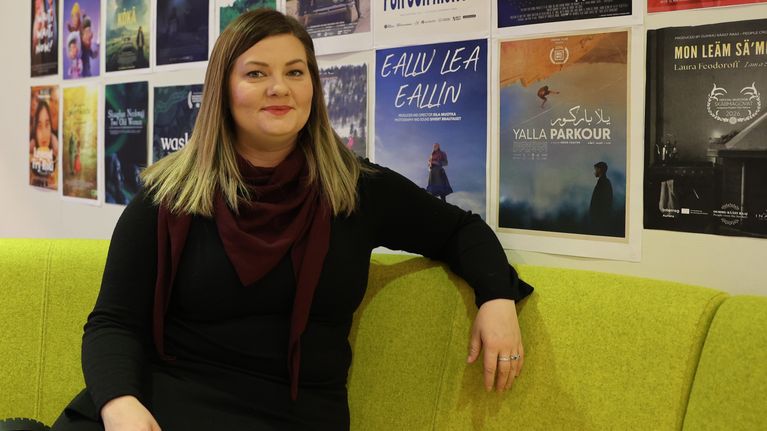 Åse Kathrin Vuolab istuu ja katsoo suoraan kameraan. Hän on luonut Heajastallan - Saamelaishäät sarjan.