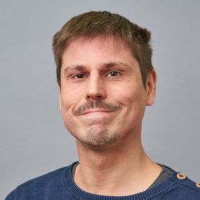 Henkilö hymyilee kameralle.