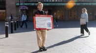 A young man holds a sign outside of Helsinki Central Railway Station.