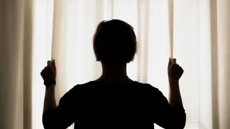 En person står vid ett fönster och tittar ut genom att hålla gardinerna.