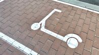 Sähköpotkulaudan parkkipaikka ladulla, valkoisella maalatut ruudun reunat ja keskellä potkulaudan kuva.