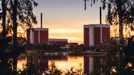Two nuclear power plants seen by a body of water, with trees on each side in the foreground. The sky and water are gold-hued.