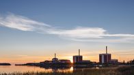 Three nuclear power plants by the water, with wispy clouds in the sky at sunset.