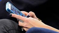 Woman's hands seen holding and using a smartphone in her lap in close-up photo.