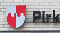 Vaaleaan tiiliseinään on kiinnitetty puna-valkoinen vaakuna ja kirjaimet Pirk.