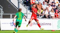 En fotbollsspelare i röd dräkt hoppar för att nicka bollen, motspelare i grönt närmar sig. 
